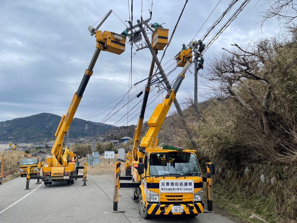 3台の高所作業車がアームを伸ばして傾いた電柱、新しく建てた電柱両方で作業している。