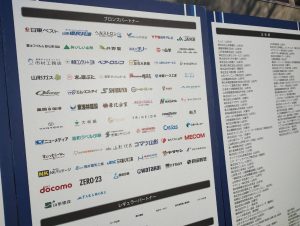 会場内に置かれたパートナー一覧が見れるボード。ブロンズパートナーの欄には68社のロゴが並んでおり、その中に渡会電気土木の会社ロゴもある。