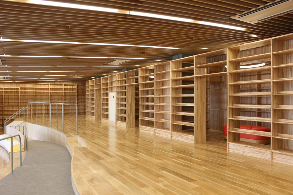 メディアセンター。壁、床、天井いずれも木材を使っている。たくさんの本棚。階段状のフロアは縁が曲線になっている。