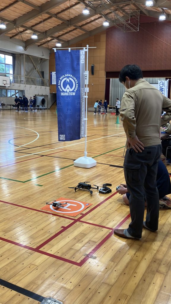 男子生徒がドローンを操縦しようとしているのを男性社員が見ている