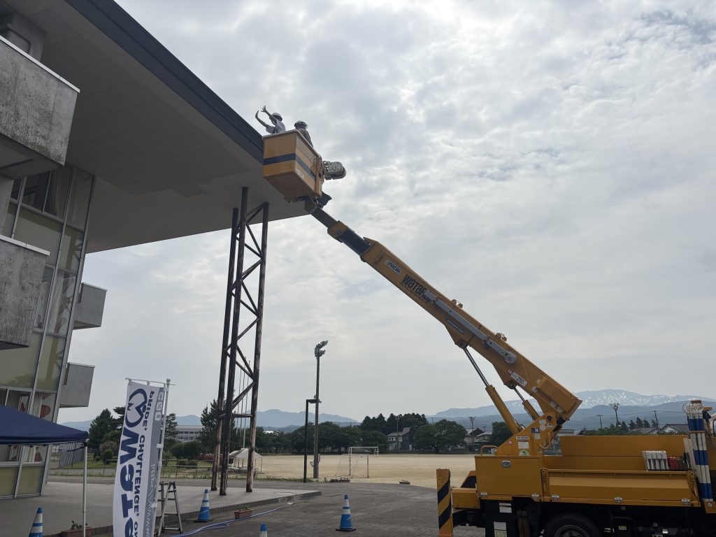 高所作業車に社員と生徒が乗っている。生徒が手を振っている