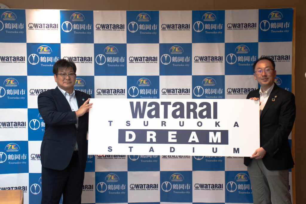 社長と市長が「WaTaRaI TSURUOKA DREAM STADIUM」のプレートを持っている写真