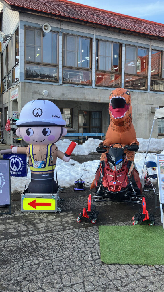 スノーモービルに恐竜の着ぐるみを着た方と記念写真